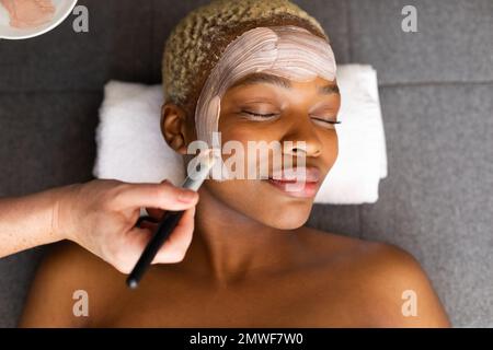 Hand of beautician giving facial to smiling african american woman with brush Stock Photo