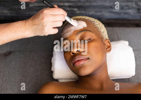 Hand of beautician giving facial to smiling african american woman with brush Stock Photo