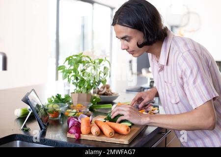 Happy biracial man cooking and using tablet in kitchen Stock Photo