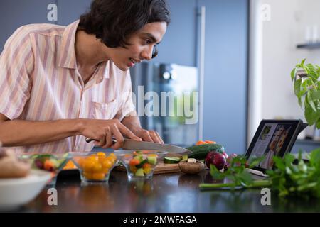 Happy biracial man cooking and using tablet in kitchen Stock Photo