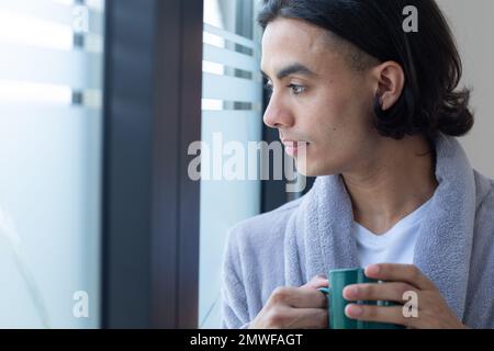 Biracial man looking through window and holding mug Stock Photo