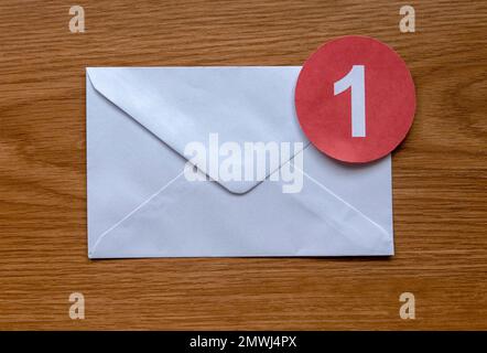 Concept of new email reminder or message alert. A white envelope with a red symbol of notification on a wooden background. Stock Photo