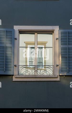 A window perfectly reflected inside of another window, amidst a dark blue wall and shutters Stock Photo