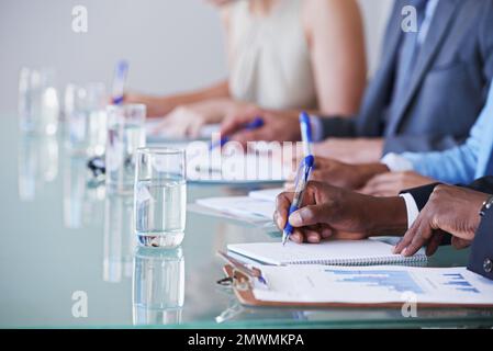 Taking notes is vital. a row of businesspeople sitting with documents in front of them in a meeting. Stock Photo