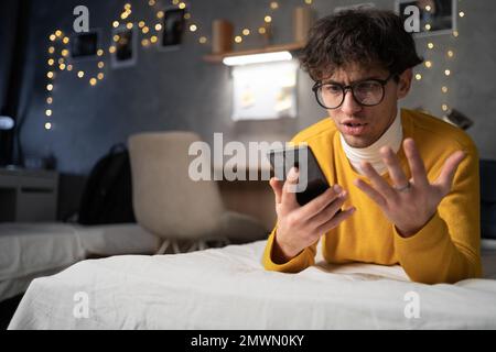 Upset frustrated male student reading bad news on message, having problem with device or Internet connection while lying on bed. Copy space Stock Photo