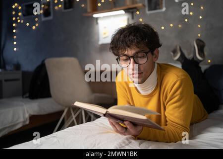 Leisure reading man is comfortable lying on her bed with a book, focused reading to prepare for a college exam. Copy space Stock Photo