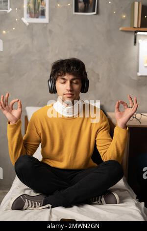 Photo of pleased arabic man meditating while sitting on bed at home room. Copy space Stock Photo