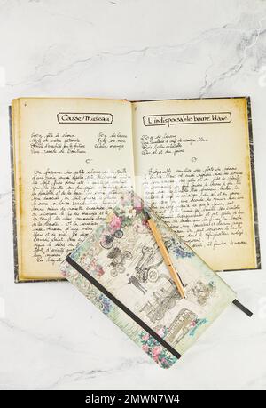 Old book with recipes in French and notebook for writing with pen on white marble. Stock Photo