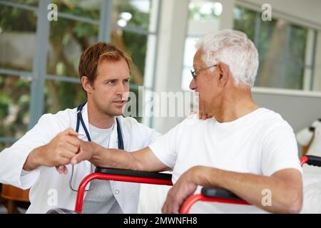 Discussing the way forward with his patient. a handsome male doctor talking to his senior patient whos in a wheelchair. Stock Photo