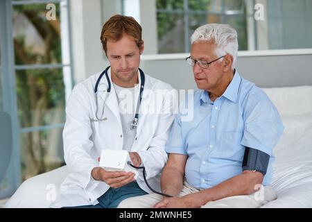 Making sure his patients blood pressure is under control. a male doctor taking his senior patients blood pressure. Stock Photo