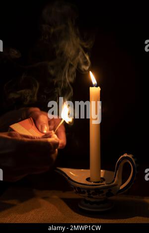 Female hands with a burning, smoldering match, next to a burning candle in the candle holder Stock Photo