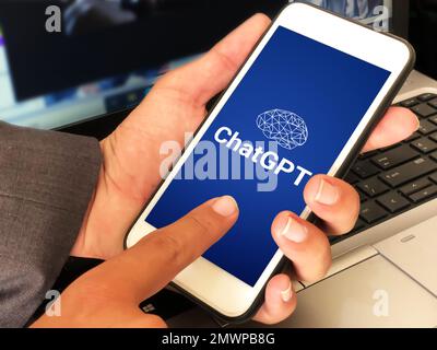 28.1. United Satates. Man using ChatGPT on Mobile with blue background and laptop in the backdrop. Modern ai writing tool using concept editorial wall Stock Photo