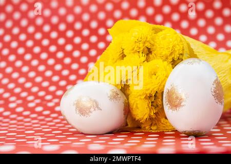 White gold eggs with bouquet of yellow chrysanthemums on red with polka dots background. Easter. Copy space Stock Photo