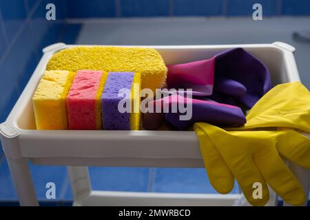 Rubber gloves and sponges on white shelf inside bathroom. Set of colorful accessory for house cleaning. Clean house Stock Photo