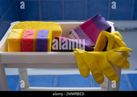 Rubber gloves and sponges on white shelf inside bathroom. Set of colorful accessory for house cleaning. Clean house Stock Photo