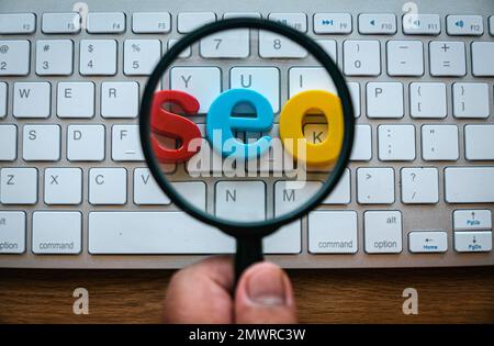 Search engine optimization concept. A hand holding magnifying glass magnify a word seo on a computer keyboard. Stock Photo