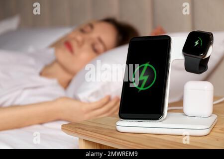 Smartphone, watch, earphones charging on wireless pad and sleeping woman in room Stock Photo