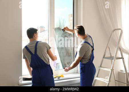 Professional workers tinting window with foil indoors Stock Photo
