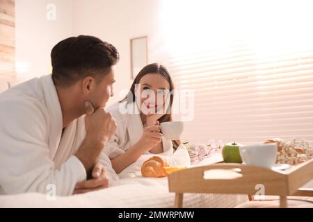 Happy couple in bathrobes having breakfast on bed at home Stock Photo