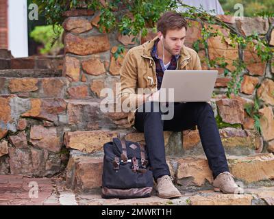 He takes his studies seriously. a handsome male student using his laptop on campus. Stock Photo