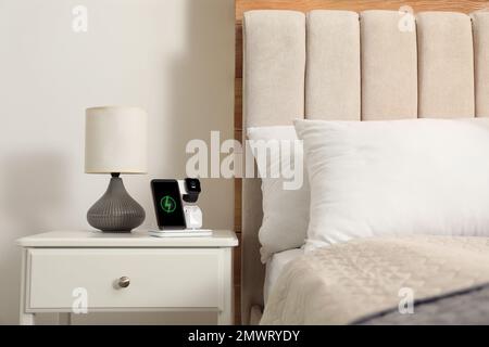 Different gadgets charging on wireless pad in bedroom Stock Photo