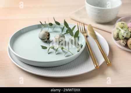 Festive Easter table setting with quail eggs and floral decoration on wooden background Stock Photo