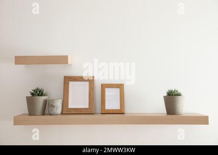 Wooden shelves with plants and photo frames  on light wall Stock Photo