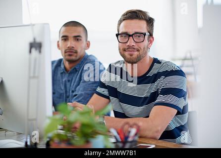Focused young pros. Portrait of two coworkers sitting at a computer in an office. Stock Photo