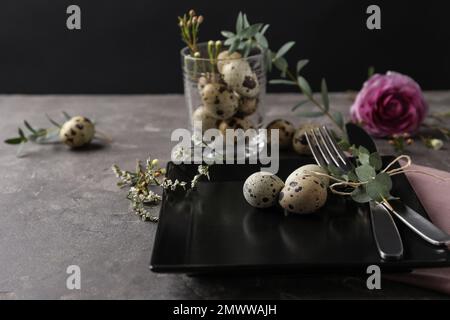 Festive Easter table setting with quail eggs and floral decoration on dark background Stock Photo