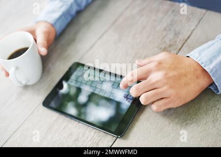 Typing in his selection. Cropped view of a mans hands using a digital tablet while sitting at a wooden table. Stock Photo
