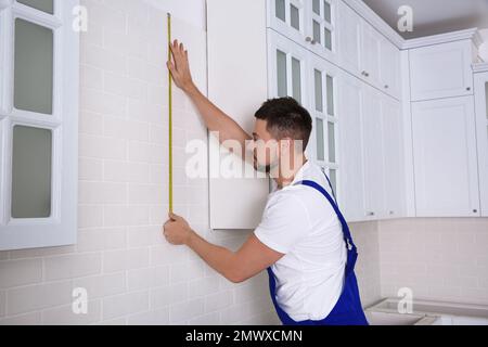Worker using measuring tape while installing new furniture in kitchen Stock Photo