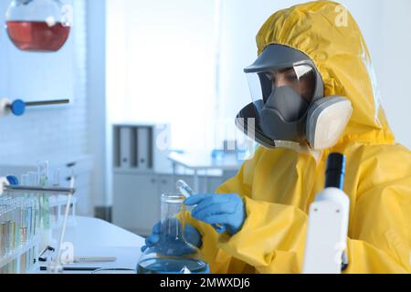 Scientist in chemical protective suit pouring reagent into flask at laboratory. Virus research Stock Photo