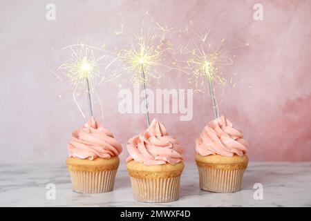 Birthday cupcakes with sparklers on table against light pink background Stock Photo