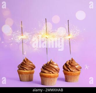 Birthday cupcakes with sparklers on violet background Stock Photo