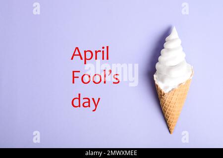 Top view of ice cream cone with shaving foam on violet background, space for text. April Fool's Day Stock Photo