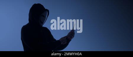 Hacker Anonymous and face mask with smartphone in hand. Man in black hood shirt holding and using mobile phone on white background. Represent cyber cr Stock Photo