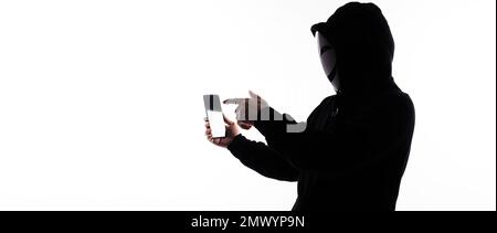 Hacker Anonymous and face mask with smartphone in hand. Man in black hood shirt holding and using mobile phone on white background. Represent cyber cr Stock Photo