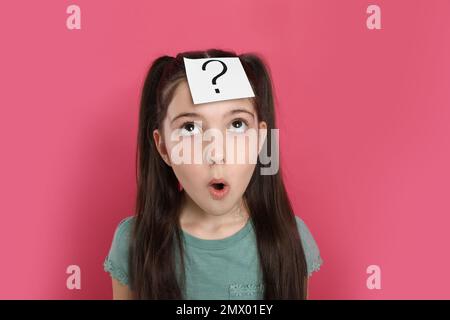 Emotional girl with question mark sticker on forehead against pink ...