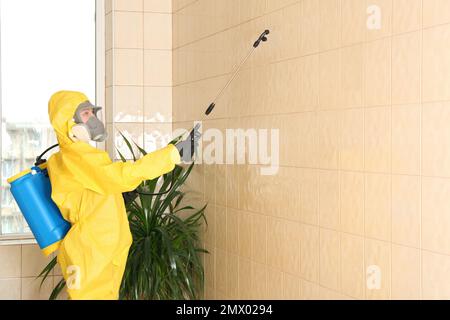 Pest control worker spraying pesticide on wall indoors. Space for text Stock Photo