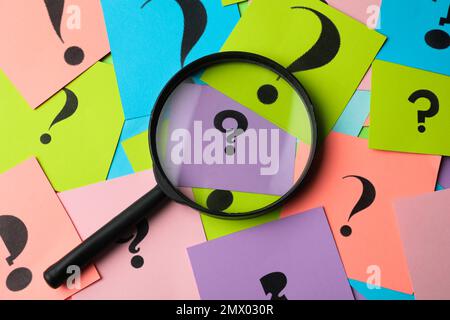 Magnifier glass on different colorful paper cards with question marks, top view Stock Photo