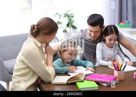 Parents helping their daughters with homework at table indoors Stock Photo