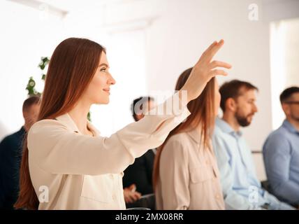 Woman raising hand to ask question at business training indoors Stock Photo