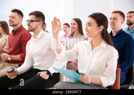 Young woman raising hand to ask question at business training indoors Stock Photo