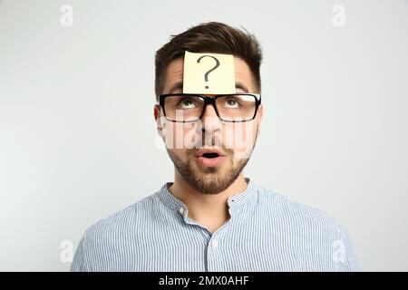 Emotional man with question mark sticker on forehead against light background Stock Photo