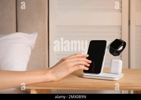 Woman taking smartphone from wireless charger in bedroom, closeup Stock Photo