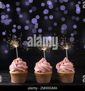 Birthday cupcakes with sparklers on wooden table against dark background Stock Photo