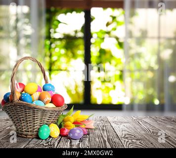 Bright Easter eggs in wicker basket on table indoors. Space for text Stock Photo