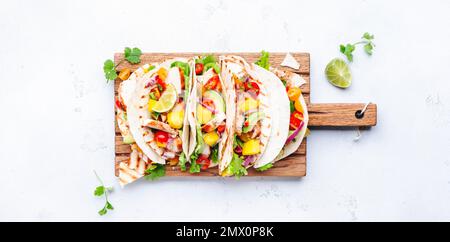 Tacos with grilled chicken, tomato salsa sauce, mango, cilantro and onion in tortilla on cutting board. White table background, top view Stock Photo