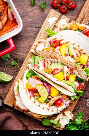 Tacos with grilled chicken, tomato salsa sauce, mango, cilantro and onion in corn tortilla on wooden board. Rustic table background, top view Stock Photo