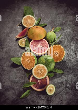 From above of various colorful citrus fruits with grapefruits and limes served on gray background with leaves in light studio Stock Photo